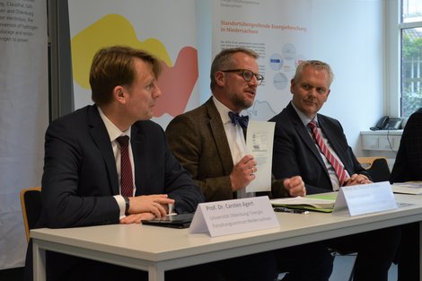 Drei Männer sitzen nebeneinander an einem Tisch bei einer Pressekonferenz